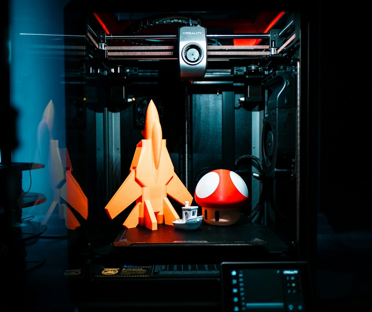 Ein 3D-Drucker mit einem orangefarbenen Raumfahrzeug und einer roten Pilzkugel.